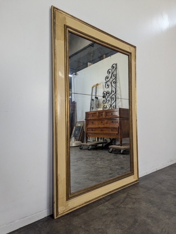 Miroir de style Louis XVI en bois laqué crème et doré à rang de perles